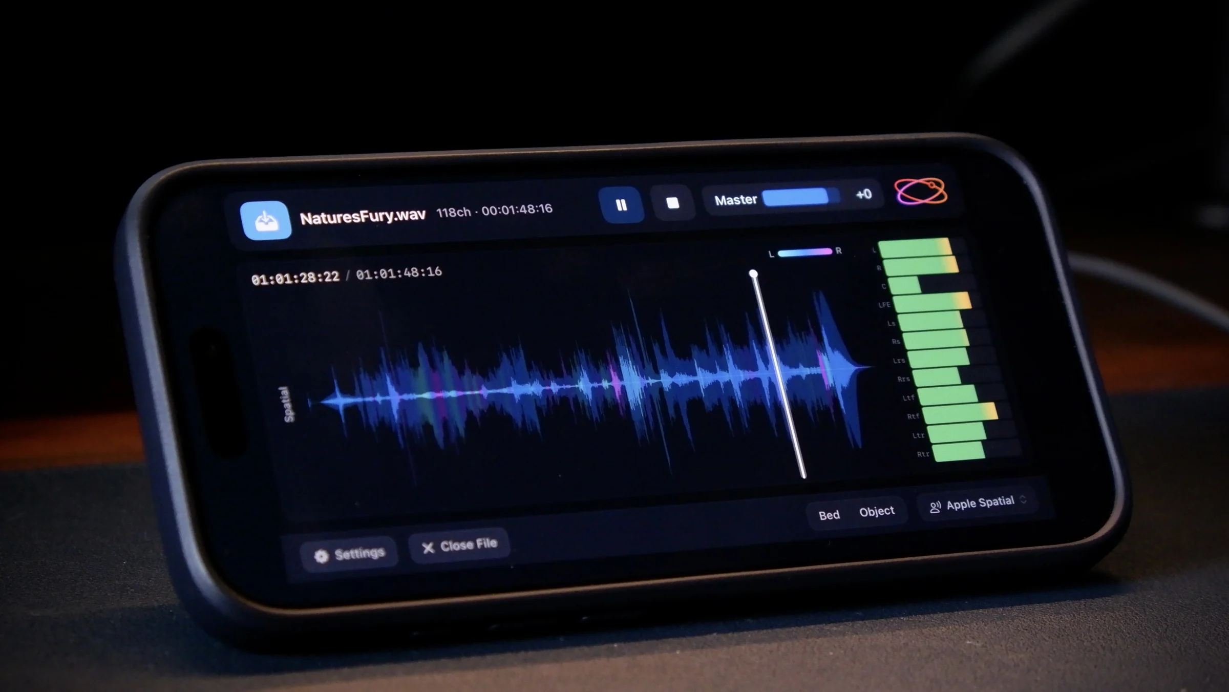 Orbit Lite on iPhone, resting on a desk, showing a spatial waveform and channel meters